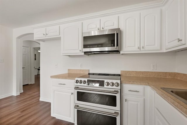 104 Live Oak Cir, Bertram, TX 78605 - kitchen with stainless steel microwave, double oven range, wood finished floors, arched walkways, and white cabinetry