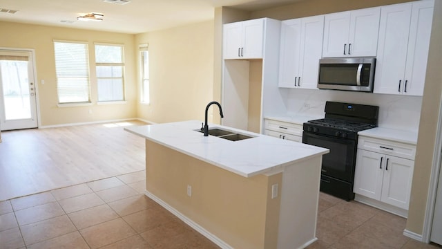 1024 Chad Loop, Round Rock, TX 78665 - kitchen with stainless steel microwave, black gas range, white cabinetry, an island with sink, and light tile patterned flooring