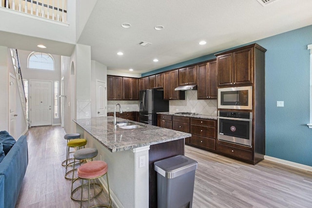 3200 Bravo Dr, Leander, TX 78641 - kitchen featuring appliances with stainless steel finishes, light wood-style floors, light stone counters, a breakfast bar area, and decorative backsplash