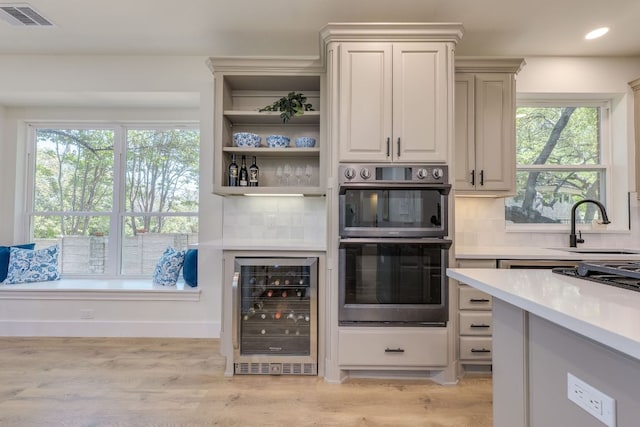 38 Cottondale Rd, The Hills, TX 78738 - kitchen featuring beverage cooler, double oven, decorative backsplash, light countertops, and light wood-type flooring