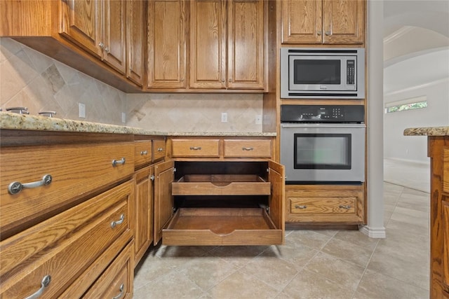 4921 Big Bend Trl, Georgetown, TX 78633 - kitchen featuring appliances with stainless steel finishes, tasteful backsplash, brown cabinets, and light stone countertops