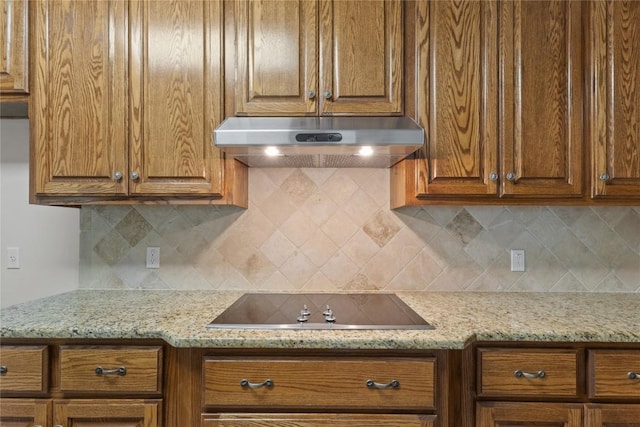 4921 Big Bend Trl, Georgetown, TX 78633 - kitchen with under cabinet range hood, black electric stovetop, tasteful backsplash, and brown cabinetry