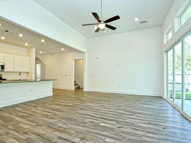 402 Zennia St, Austin, TX 78751 - unfurnished living room with light wood finished floors, stairs, a ceiling fan, recessed lighting, and a high ceiling