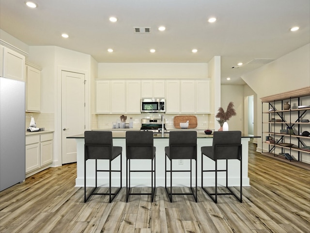 402 Zennia St, Austin, TX 78751 - kitchen featuring stainless steel appliances, light wood finished floors, backsplash, white cabinets, and recessed lighting