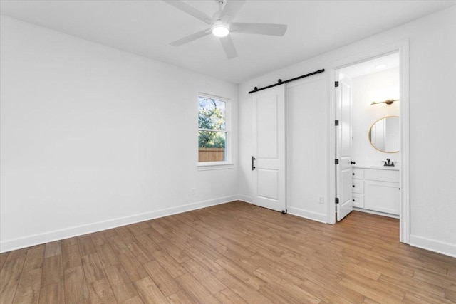4121 Turning Leaf Dr, Nolanville, TX 76559 - unfurnished bedroom featuring a barn door, light wood finished floors, ensuite bath, and a ceiling fan