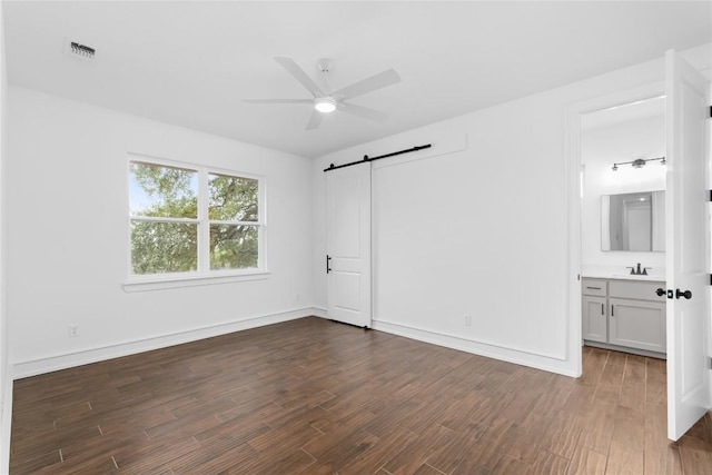 7026 Troyan, Temple, TX 76502 - unfurnished bedroom with a barn door, dark wood-style flooring, connected bathroom, and ceiling fan
