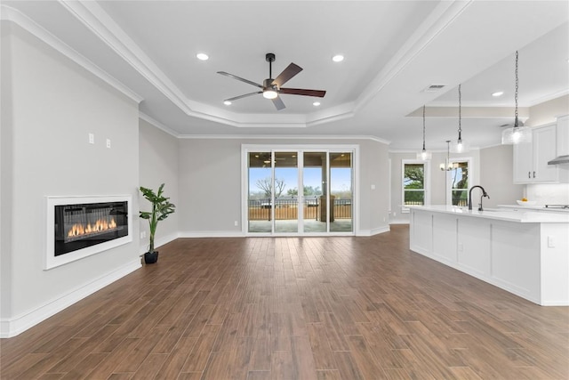 7026 Troyan, Temple, TX 76502 - unfurnished living room featuring a tray ceiling, a ceiling fan, a glass covered fireplace, dark wood-style flooring, and ornamental molding