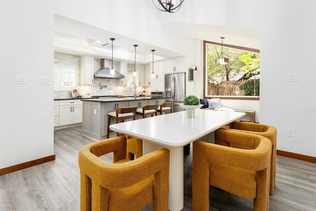 4604 Fawnwood Cv, Austin, TX 78735 - kitchen featuring stainless steel fridge with ice dispenser, wall chimney range hood, a kitchen island with sink, a kitchen breakfast bar, and light wood finished floors