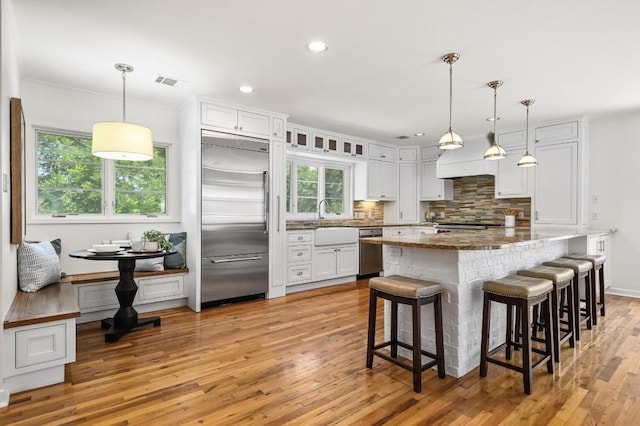 2507 Hartford Rd, Austin, TX 78703 - kitchen featuring appliances with stainless steel finishes, backsplash, white cabinetry, a breakfast bar area, and light wood-style flooring