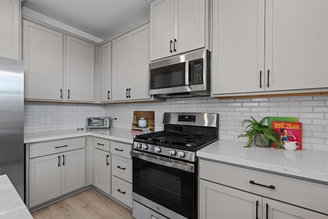 13506 Grand Central Dr, Pflugerville, TX 78660 - kitchen with appliances with stainless steel finishes, decorative backsplash, light wood-type flooring, light stone countertops, and gray cabinets