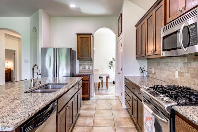 5521 Texas Bluebell Dr, Spicewood, TX 78669 - kitchen featuring stainless steel appliances, arched walkways, decorative backsplash, light stone counters, and light tile patterned floors