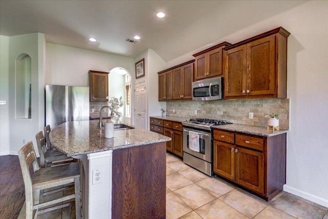 5521 Texas Bluebell Dr, Spicewood, TX 78669 - kitchen with stainless steel appliances, decorative backsplash, light stone countertops, an island with sink, and a breakfast bar area