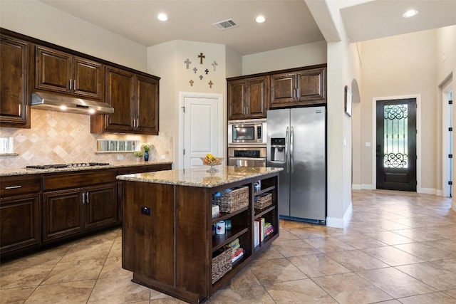 8709 Fescue Ln, Austin, TX 78738 - kitchen featuring appliances with stainless steel finishes, under cabinet range hood, light stone countertops, arched walkways, and decorative backsplash