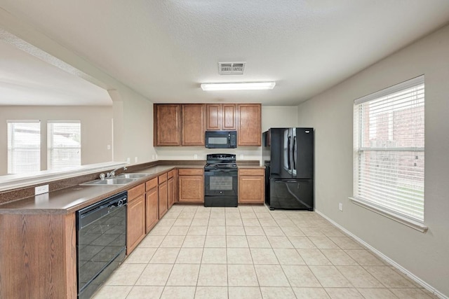 3417 Tralagon Trl, Pflugerville, TX 78660 - kitchen with black appliances, a peninsula, light tile patterned floors, dark countertops, and brown cabinets