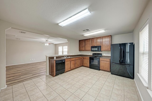 3417 Tralagon Trl, Pflugerville, TX 78660 - kitchen with black appliances, a peninsula, brown cabinetry, light tile patterned flooring, and ceiling fan