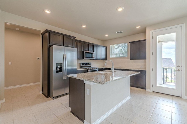116 Mulligan Dr Unit 103, San Marcos, TX 78666 - kitchen with appliances with stainless steel finishes, backsplash, light stone countertops, an island with sink, and light tile patterned floors