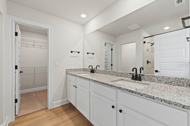 9517 Balmy Ln, Manor, TX 78653 - bathroom featuring double vanity, a tile shower, wood finished floors, a walk in closet, and recessed lighting