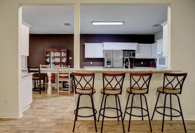 128 Moku Manu Dr, Bastrop, TX 78602 - kitchen with stainless steel appliances, light wood-style flooring, white cabinetry, and a peninsula