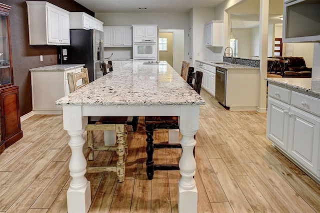 128 Moku Manu Dr, Bastrop, TX 78602 - kitchen featuring stainless steel appliances, light wood-type flooring, a kitchen island, white cabinets, and light stone countertops