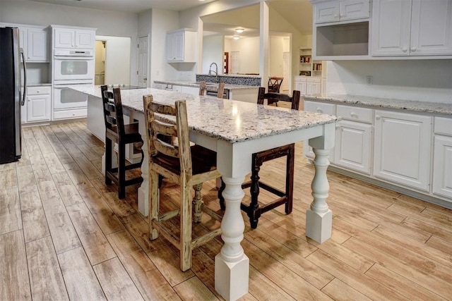 128 Moku Manu Dr, Bastrop, TX 78602 - kitchen featuring freestanding refrigerator, white double oven, light wood-style flooring, and a breakfast bar