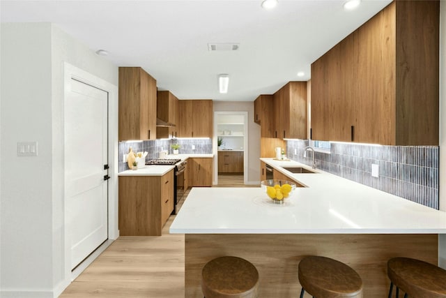 1806 Teton Dr, Austin, TX 78757 - kitchen with brown cabinets, range with gas cooktop, a peninsula, light countertops, and decorative backsplash