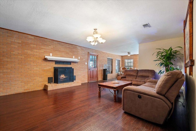 3704 Austin Cv, Lago Vista, TX 78645 - living room featuring wood finished floors, a chandelier, a brick fireplace, brick wall, and a textured ceiling