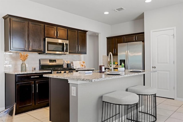 2010 Grow Ln, Austin, TX 78754 - kitchen with appliances with stainless steel finishes, light tile patterned floors, a kitchen island with sink, light stone counters, and recessed lighting