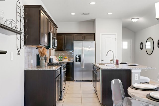 2010 Grow Ln, Austin, TX 78754 - kitchen with appliances with stainless steel finishes, decorative backsplash, dark brown cabinetry, a center island with sink, and light stone countertops