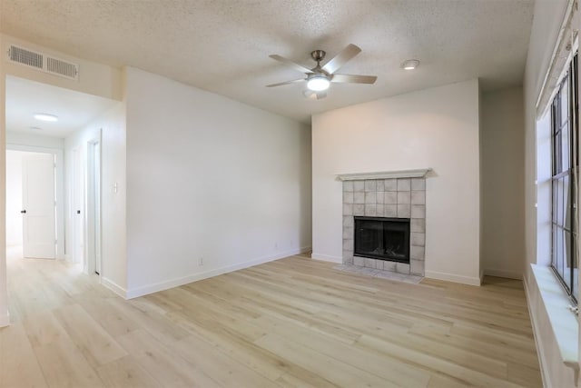 203 E 31st St Unit 206, Austin, TX 78705 - unfurnished living room with a textured ceiling, ceiling fan, light wood-style floors, a tiled fireplace, and plenty of natural light
