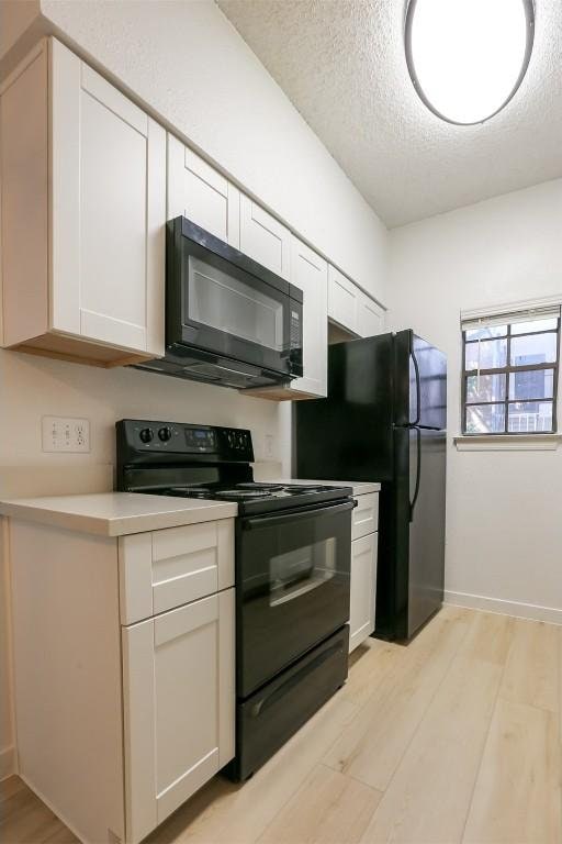 203 E 31st St Unit 206, Austin, TX 78705 - kitchen featuring black appliances, a textured ceiling, white cabinets, light wood finished floors, and light countertops