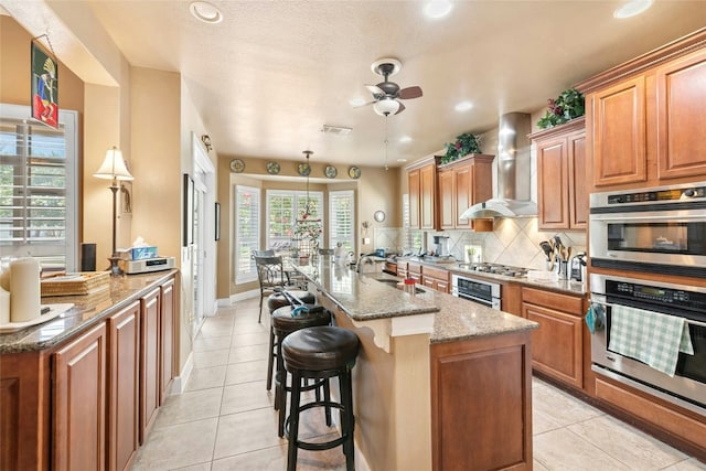 207 Breezeway Ln, Georgetown, TX 78633 - kitchen featuring wall chimney range hood, stainless steel appliances, ceiling fan, stone counters, and backsplash