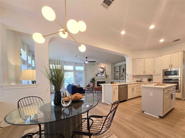 10303 Spicewood Pkwy, Austin, TX 78750 - kitchen with appliances with stainless steel finishes, light wood-style flooring, light countertops, a fireplace, and white cabinetry