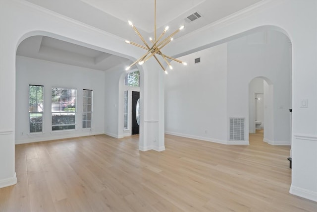 10303 Spicewood Pkwy, Austin, TX 78750 - unfurnished living room featuring healthy amount of natural light, arched walkways, light wood-style flooring, a tray ceiling, and crown molding