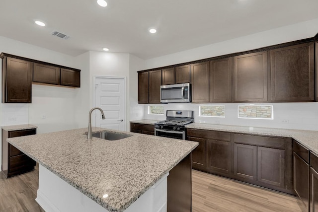 16817 Ponte Cv, Pflugerville, TX 78660 - kitchen with stainless steel appliances, light wood-style floors, dark brown cabinetry, light stone countertops, and a center island with sink