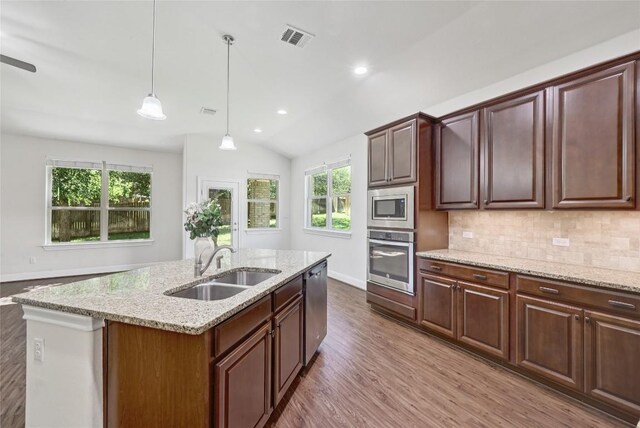 2232 Skippy Cv, Leander, TX 78641 - kitchen featuring stainless steel appliances, wood finished floors, light stone countertops, backsplash, and a kitchen island with sink