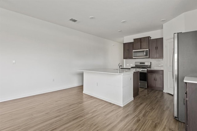 11825 Monterosso Dr, Austin, TX 78754 - kitchen with appliances with stainless steel finishes, wood finished floors, dark brown cabinetry, tasteful backsplash, and light countertops