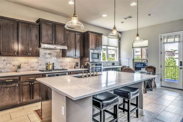 110 Waverly Spire Ct, Austin, TX 78738 - kitchen with stainless steel appliances, decorative backsplash, under cabinet range hood, a kitchen island with sink, and recessed lighting
