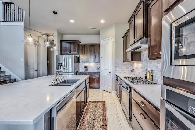 110 Waverly Spire Ct, Austin, TX 78738 - kitchen featuring appliances with stainless steel finishes, under cabinet range hood, backsplash, dark brown cabinets, and decorative light fixtures