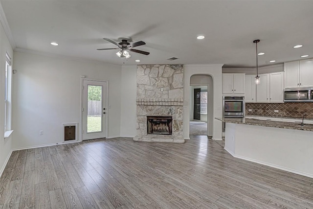 1512 Berlin Ln, Austin, TX 78753 - unfurnished living room with ceiling fan, a stone fireplace, light wood-style floors, crown molding, and arched walkways