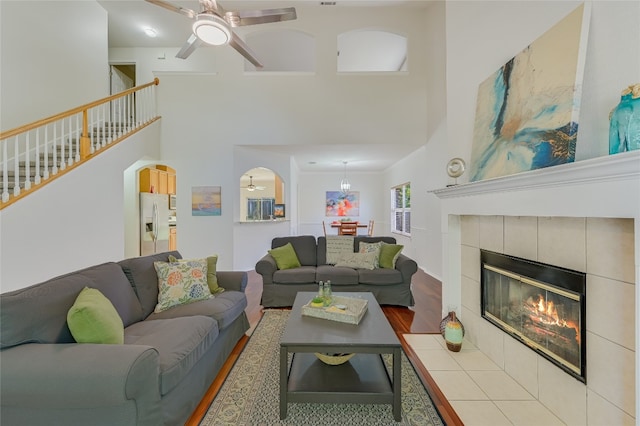 7008 Wandering Oak Rd, Austin, TX 78749 - living room featuring a towering ceiling, wood finished floors, a ceiling fan, stairs, and a tile fireplace