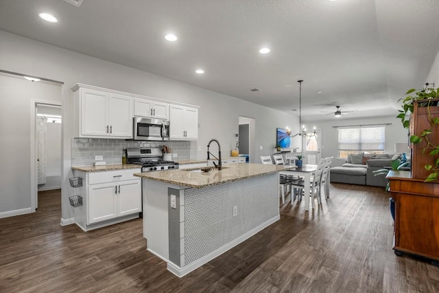 13911 Macquarie Dr, Pflugerville, TX 78660 - kitchen with appliances with stainless steel finishes, a ceiling fan, dark wood-type flooring, light stone counters, and a kitchen island with sink