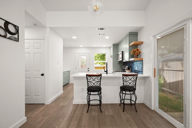 7913 W Gate Blvd Unit A, Austin, TX 78745 - kitchen with stainless steel microwave, open shelves, light countertops, wood finished floors, and a peninsula