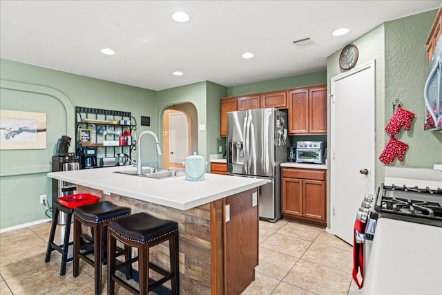 kitchen featuring appliances with stainless steel finishes, light tile patterned flooring, brown cabinetry, a kitchen island with sink, and recessed lighting