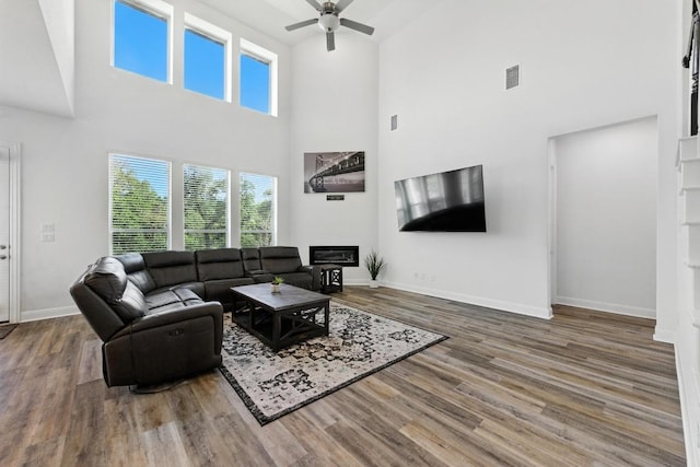216 Tovas Secret Cv, Georgetown, TX 78628 - living room featuring a towering ceiling, a ceiling fan, wood finished floors, and a glass covered fireplace
