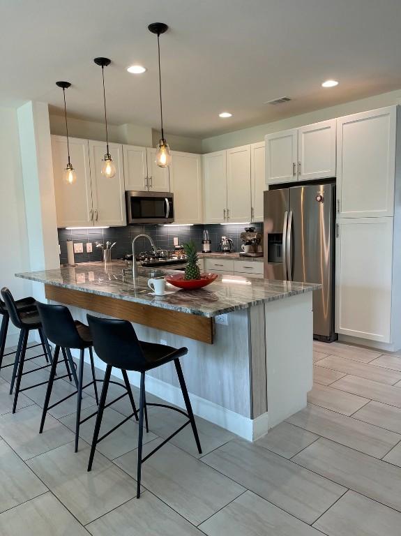 300-304 Tesla Cir, Austin, TX 78681 - kitchen featuring stainless steel appliances, dark stone countertops, a peninsula, tasteful backsplash, and white cabinetry