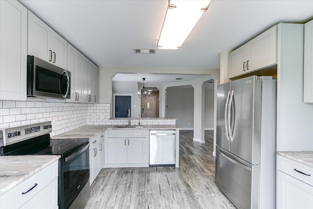 1000 Warbler Cv, Hutto, TX 78634 - kitchen with appliances with stainless steel finishes, tasteful backsplash, light wood-style floors, a chandelier, and a peninsula