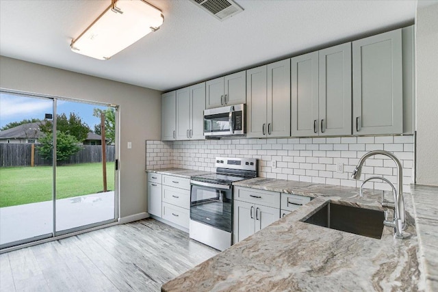 1000 Warbler Cv, Hutto, TX 78634 - kitchen with appliances with stainless steel finishes, decorative backsplash, light stone counters, light wood finished floors, and gray cabinets