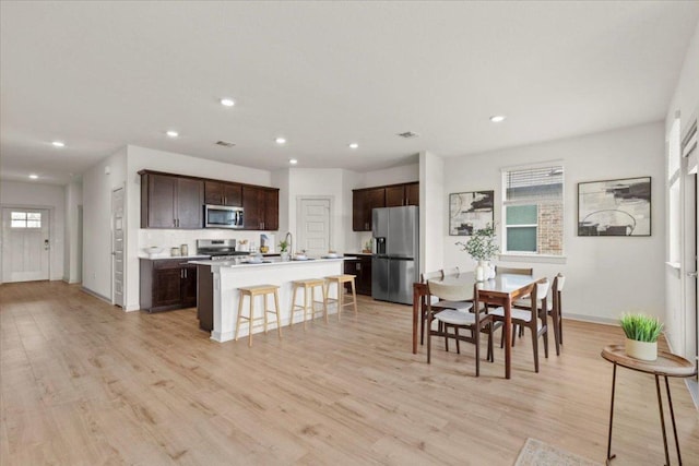 10708 Defender Trl, Austin, TX 78754 - kitchen with stainless steel appliances, dark brown cabinetry, a kitchen island with sink, light wood-type flooring, and recessed lighting