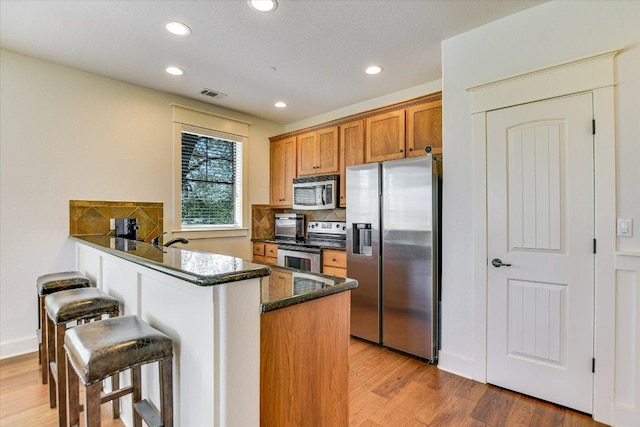 6608 Lantern View Dr Unit 102, Jonestown, TX 78645 - kitchen with stainless steel appliances, brown cabinets, recessed lighting, light wood-style floors, and tasteful backsplash