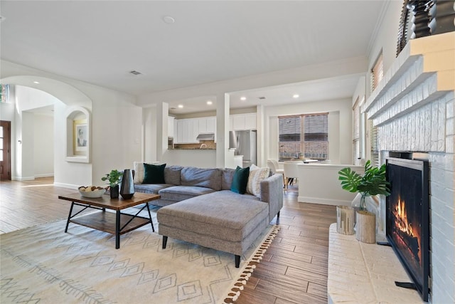3121 Yandall Dr, Austin, TX 78748 - living room with a brick fireplace, light wood-style flooring, crown molding, arched walkways, and recessed lighting